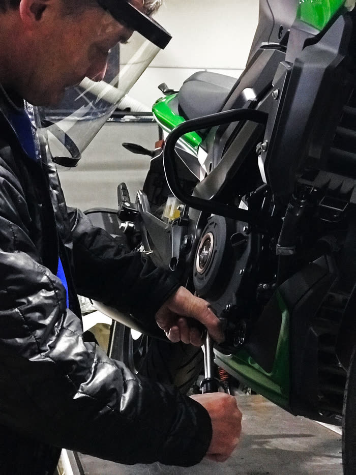 Mecánico de For Export con máscara de protección, ajustando una Bajaj Dominar verde en el taller